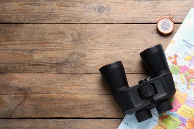 Modern binoculars, map and compass on wooden table, flat lay. Space for text
