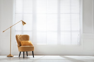 Photo of Cosy armchair and floor lamp near large window with blinds in spacious room. Interior design