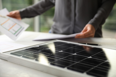 Solar panel and blurred person with papers on background, closeup