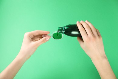 Woman pouring cough syrup into dosing spoon on green background, closeup