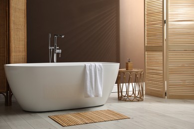 Modern ceramic bathtub and small table near brown wall in room
