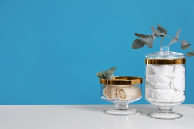 Jars with cotton pads and luffa sponges on white table against blue background. Space for text