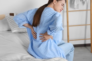 Woman suffering from back pain while sitting on bed at home. Symptom of scoliosis