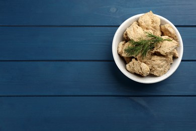 Dehydrated soy meat chunks with dill in bowl on blue wooden table, top view. Space for text