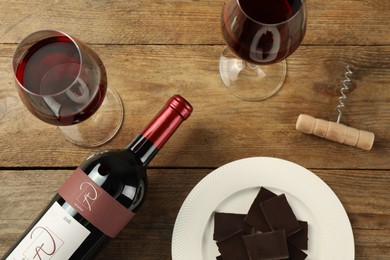 Flat lay composition with tasty red wine and chocolate on wooden table