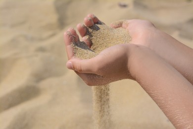 Child pouring sand from hands outdoors, closeup. Fleeting time concept