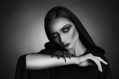 Mysterious witch with spooky spider on dark background. Black and white effect