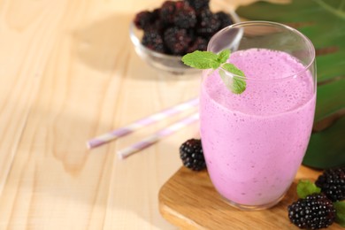Delicious blackberry smoothie in glass and berries on wooden table, space for text