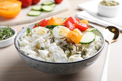 Fresh cottage cheese with vegetables, seeds and eggs in bowl on wooden table, closeup