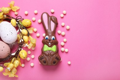 Photo of Flat lay composition with chocolate Easter bunny, festively decorated eggs and candies on pink background. Space for text