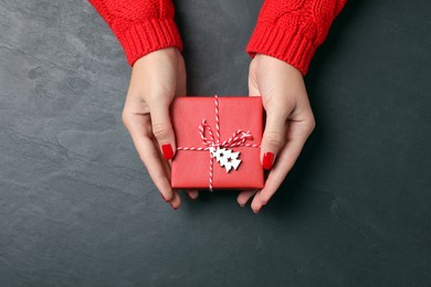 Christmas present. Woman with gift box at black table, top view