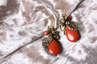 Beautiful pair of metal earrings with red jasper gemstones on light fabric, above view