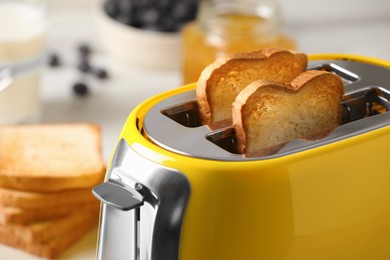 Modern yellow toaster with roasted bread slices on table, closeup