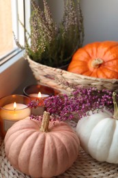 Wicker basket with beautiful heather flowers, pumpkins and burning candles near window indoors
