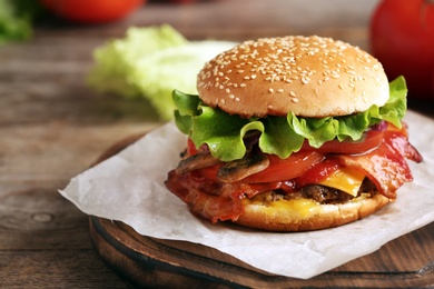 Tasty burger with bacon on wooden table. Space for text