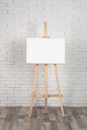Wooden easel with blank canvas near white brick wall