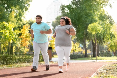 Overweight couple running together in park on sunny day