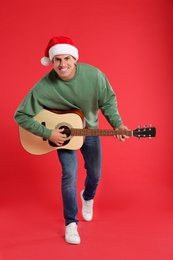 Man in Santa hat playing acoustic guitar on red background. Christmas music