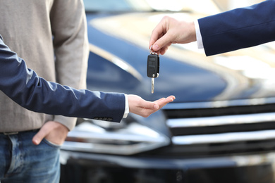 Photo of Salesman giving key to customers in modern auto dealership, closeup. Buying new car