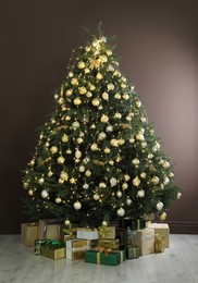 Beautifully decorated Christmas tree and many gift boxes near brown wall indoors