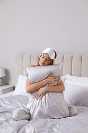 Beautiful woman hugging pillow on comfortable bed with silky linens