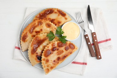 Delicious fried chebureki with sauce served on white table, top view