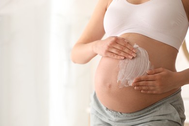 Young pregnant woman applying cosmetic product on belly in bathroom, closeup. Space for text