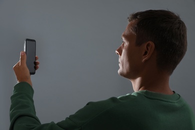 Man unlocking smartphone with facial scanner on grey background. Biometric verification