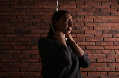 Depressed woman with rope noose on neck near brick wall