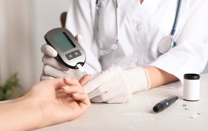 Doctor checking blood sugar level with glucometer at table. Diabetes test