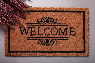 Photo of Doormat with word Welcome and heather flowers on grey background, flat lay