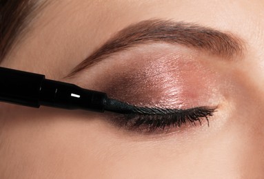 Beautiful woman applying black eyeliner, closeup view