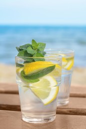 Photo of Refreshing water with lemon and mint on wooden table outdoors