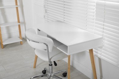 Stylish workplace with white desk and comfortable chair near window indoors. Interior design