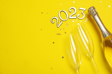 Happy New Year 2023! Flat lay composition with bottle of sparkling wine on yellow background, space for text