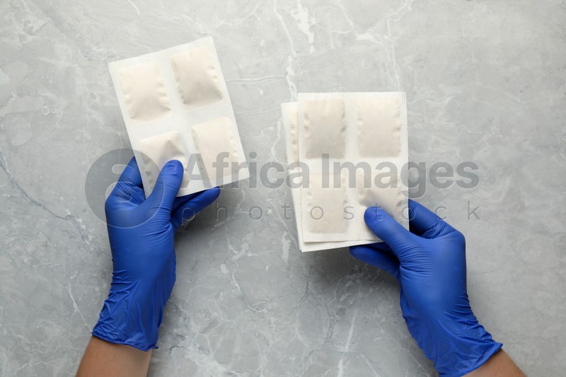 Man in gloves with mustard plasters at light grey marble table, top view