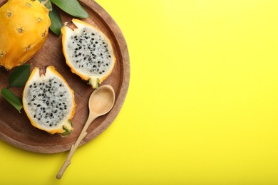 Photo of Wooden plate with delicious cut and whole dragon fruits (pitahaya) on yellow background, top view. Space for text