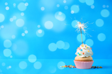 Birthday cupcake with sparkler on light blue background, space for text. Bokeh effect