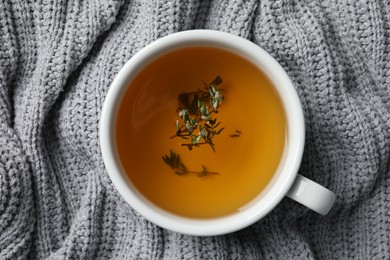 Photo of Cup of fresh thyme tea on light gray knitted blanket, top view