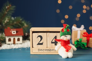 Christmas Eve - December 24. Block calendar and cute toy snowman on light blue wooden table