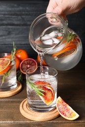 Woman pouring refreshing drink with sicilian orange from jug into glass at wooden table, closeup