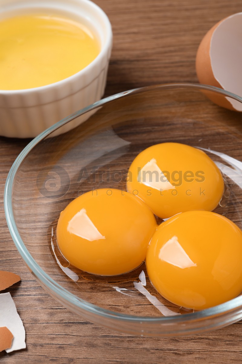 Bowls with raw egg yolks on wooden table, closeup