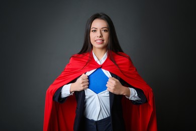 Confident businesswoman wearing superhero costume under suit on grey background