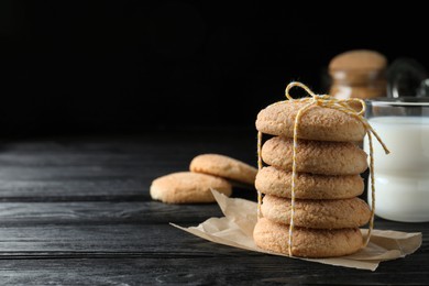 Photo of Delicious sugar cookies and glass of milk on black wooden table, space for text