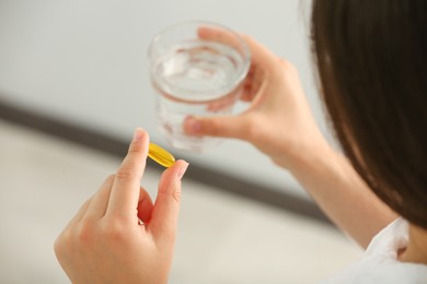 Young woman with glass of water and dietary supplement pill indoors, closeup