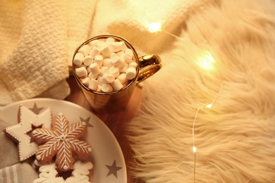 Cup of hot drink with marshmallows, cookies and Christmas lights on table, above view