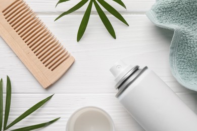 Dry shampoo spray, comb, towel and green twigs on white wooden table, flat lay