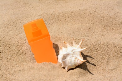 Bottle with sun protection spray and seashell on sandy beach