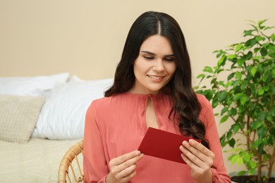 Photo of Young woman with greeting card in living room, space for text