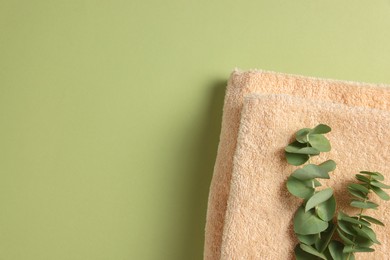 Soft folded towels with eucalyptus branch on green background, top view. Space for text
